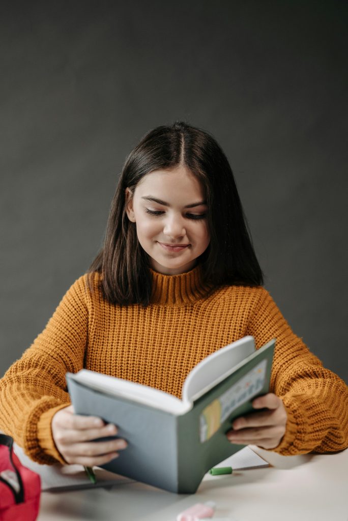 Teen girl in brown sweater reading happily indoors, emphasizing education and study.
