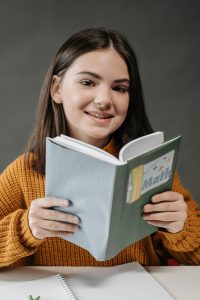 Teen girl smiling while holding a math book, showcasing her love for learning in a classroom setting.